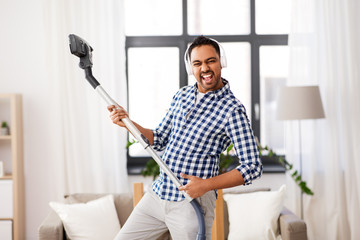 Sticker - household and cleaning concept - indian man in headphones with vacuum cleaner having fun at home