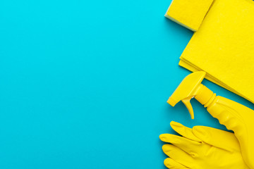 yellow cleanser in plastic container with spray, rubber protective gloves, sponge and cloths for cleaning on the turquoise blue background. flat lay image of yellow cleaning products with copy space