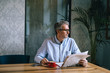 © cherryandbees - middle aged gray haired man reading newspaper and drinking coffee in cafe bar