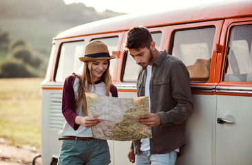 Wall Mural - A young couple on a roadtrip through countryside, looking at a map.