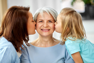 family, generation and female concept - mother and daughter kissing happy grandmother at home