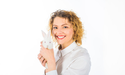 Happy woman holds white small hare on hands. Smiling girl hugs baby bunny rabbit. Beautiful woman gently hugs bunny. Cute Easter bunny. Woman stroking rabbit. Blonde girl in white shirt holds rabbit.