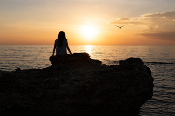 Wall Mural - silhouette of a young girl. sits and watches the beautiful sunset on the sea.