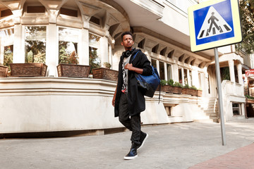 Handsome student outside walking on street, in casual clothes with backpack and headset, near crosswalk, copy space.