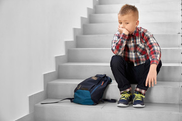 Lonely schoolboy sitting on stairwell in school, thinking.