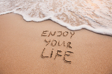 Enjoy your life, happiness concept, positive thinking, inspirational quote written on sand beach.