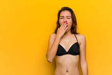 Wall Mural - Young european woman wearing bikini yawning showing a tired gesture covering mouth with her hand.