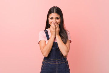 Wall Mural - Young pretty arab woman wearing a jeans dungaree laughing about something, covering mouth with hands.