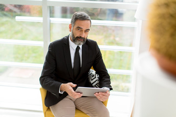 Wall Mural - Handsome smiling mature businessman with tablet in the office working, reading or searching something