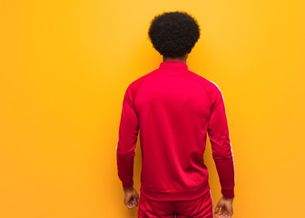 Wall Mural - Young sport black man over an orange wall from behind, looking back