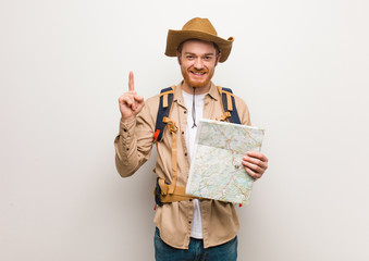 young redhead explorer man showing number one. holding a map.