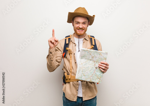 Cuadros en Lienzo Young redhead explorer man showing number one. Holding a map.