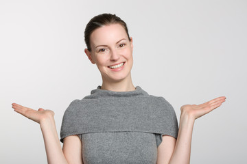 young smiling woman in grey sweater makes a not know gesture with her arms