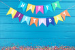 Paper flags with text Happy Birthday and sweet sprinkles on blue background