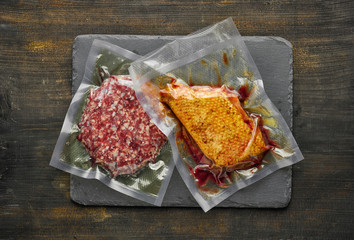 Wall Mural - Duck breast and burger meat vacuum sealed ready for sous vide cooking on wooden table, from above