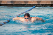 © colloidial - Young man swimming butterfly on a sunny day.  Deep blue pool water.  Black and blue lane lines.  Blue goggles, no swim cap.