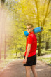 © Olha - Young sports man in red t-shirt standing on the park track and posing with a blue yoga mat. Behind it a blurred background
