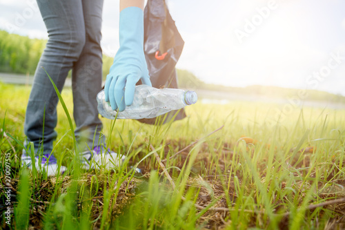 Fotografía Photo of side of woman in rubber gloves picking up garbage in bag on banks of river