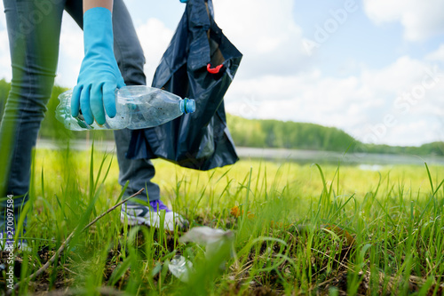 Cuadros en Lienzo Photo of side of girl in rubber gloves picking up garbage in bag on banks of river