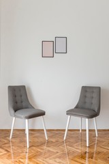 two vintage chairs in white room with two image frames on wall