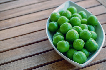 Green plums in white dish on wooden background close up view with copyspace