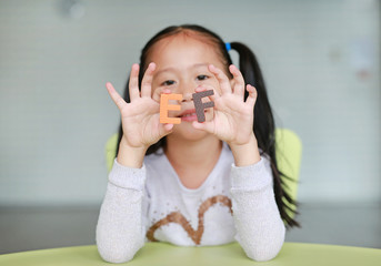 Wall Mural - Adorable little Asian child girl holding alphabet EF (Executive Functions) text on her face. Education concept.