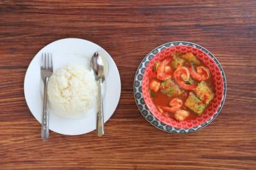 Wall Mural - Delicious Thai yellow curry with shrimp and fried herb vegetable omelet in bowl served with jasmine rice on wooden table background. Top view.