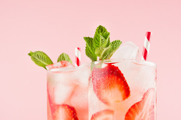 Fresh strawberry cocktailы with spiced berries, ice cubes, mint and striped straw on soft pink color, closeup, top section, edge.