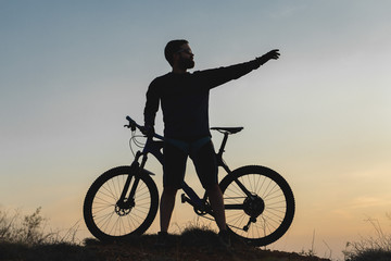 Cyclist in shorts and jersey on a modern carbon hardtail bike with an air suspension fork rides off-road on the orange-red hills at sunset evening in summer