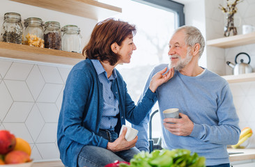 A portrait of senior couple in love indoors at home, holding coffee.