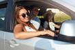 © artiemedvedev - Group of friends rented a car on summer road trip and arrived to the sea beach. Woman in glasses looks out of the car window. Passanger girl having fun with friends in vehicle. Travel lifestyle.