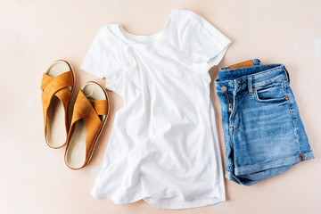 Woman's casual summer vacation outfits with white t-shirts, denim shorts, trendy leather sandals, with crisscross details on pink pastel background.