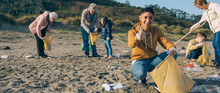 Young Man Picking Up Trash With Group Of Volunteers On The Beach