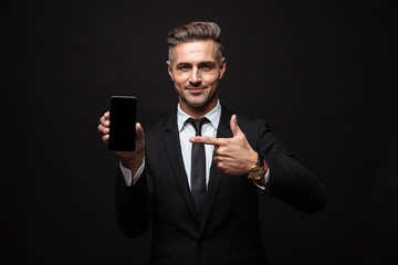 Wall Mural - business man posing isolated over black wall background using mobile phone showing display.