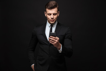 Sticker - Business man posing isolated over black wall background using mobile phone.