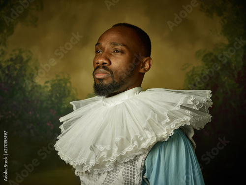 Cuadros en Lienzo Young man as a medieval grandee or nobleman on dark studio background