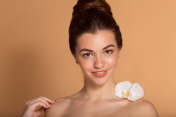 Closeup portrait of young beautiful girl with flawless skin with white orchid flower on her shoulder. Skin care, beauty and cosmetics concept.