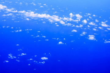 view of the window of airplane seeing blue sky, white cloud and deep blue sea.