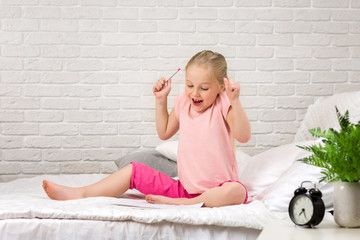 cute happy little girl drawing pictures while lying on bed. kid painting at home