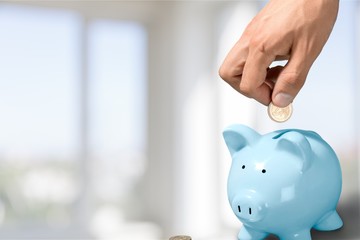 Hand putting coin to piggy bank and coins on white background