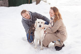 Fototapeta Las - Happy young married couple hugging their smart big white dog while walking in the winter. Family pastime concept