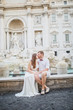 young beautiful couple in white clothes stands near Trevi Fountain in Rome in Italy