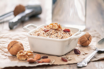 Oatmeal with walnuts, raisins and almonds in a white ceramic bowl on a vintage rustic wood background. Healthy nutrition breakfast concept.