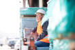 © Westend61 - Woman wearing reflective vest and hard hat sitting on building material