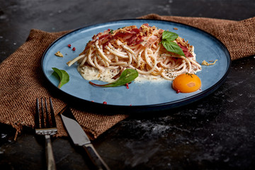 Wall Mural - Classic pasta carbonara with yolk on a plate. Pasta laid out on a blue plate on a dark background. Concept of Italian cuisine, beautiful serving dishes, close-up.