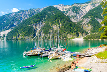 ACHENSEE LAKE, AUSTRIA - JUL 31, 2018: Couple Of People Relaxing Under Sun Umbrella On Shore Of Achensee Lake With Yacht Marina Near Pertisau Town On Sunny Summer Day, Tirol, Austria.