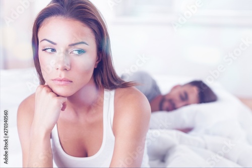 Photographie Dissatisfied beautiful young woman in bed with sad expression on her face, sex problems in long relationship or marriage while man sleeping