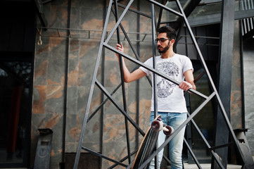 Wall Mural - Street style arab man in eyeglasses with longboard posed inside metal pyramid construction.