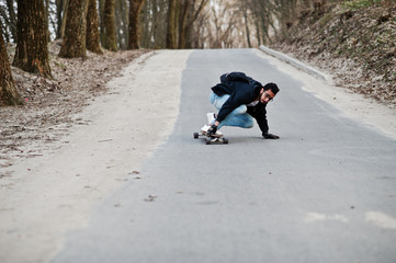 Wall Mural - Street style arab man in eyeglasses with longboard longboarding down the road.