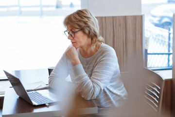 Wall Mural - middle-aged woman business in workplace in cafe, office, she's working on her laptop.